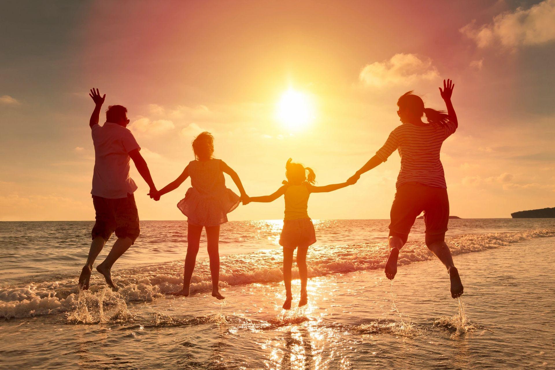 A joyful family leaps into the air on the beach, silhouetted against a vibrant sunset sky