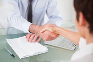 A man and woman shaking hands over a desk, symbolizing agreement and collaboration in a professional setting